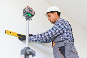 een Indisch arbeider werken in een leeg appartement. een Mens in een uniform maakt reparaties binnen de gebouw foto