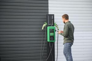 Mens Holding macht opladen kabel voor elektrisch auto in buitenshuis auto park foto
