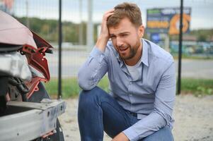 een gefrustreerd Mens in de buurt een gebroken auto. gepakt mijn hoofd realiseren de schade is echt, de auto is verder reparatie foto