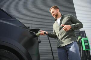 Mens Holding macht opladen kabel voor elektrisch auto in buitenshuis auto park foto