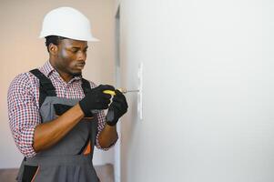 Afro-Amerikaans elektricien gebruik makend van stopcontact Spanning regelgever in kamer foto