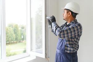 Indisch werkman in overall installeren of aanpassen plastic ramen in de leven kamer Bij huis foto