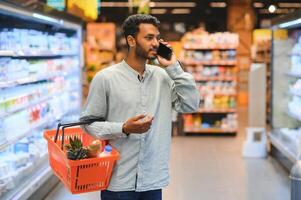 Indisch Mens gebruik makend van smartphone Bij kruidenier winkel. foto