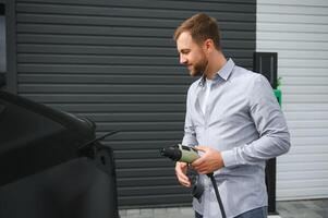 Mens Holding macht opladen kabel voor elektrisch auto in buitenshuis auto park foto