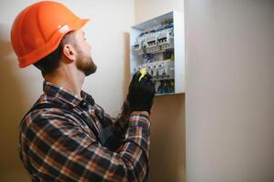 een mannetje elektricien werken in een schakelbord met een elektrisch Verbinden kabel foto