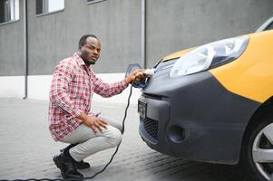 portret van een jong Afrikaanse Mens staand met opladen kabel in de buurt de opladen station. foto