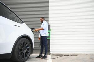 Mens aansluiten in elektrisch auto buiten kantoor in auto park opladen foto