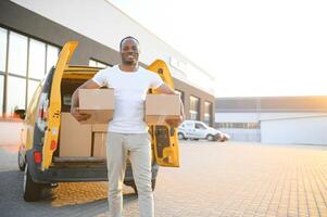 portret van een jong Afrikaanse Amerikaans pakket levering Mens in de buurt een auto met dozen. foto