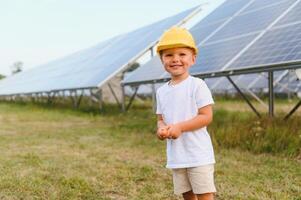 portret van een kind in de buurt de zonne- panelen. een weinig jongen in een beschermend helm in de buurt zonne- panelen met zijn hand. het schieten Bij een zonne- macht fabriek. ecologisch boerderij. zonne- macht station. mensen foto