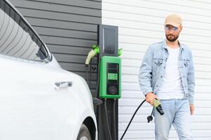 Mens Holding macht opladen kabel voor elektrisch auto in buitenshuis auto park. en hij s gaan naar aansluiten de auto naar de opladen station in de parkeren veel in de buurt de boodschappen doen centrum. foto