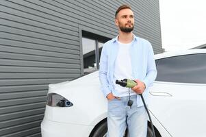 Mens Holding macht opladen kabel voor elektrisch auto in buitenshuis auto park. en hij s gaan naar aansluiten de auto naar de opladen station in de parkeren veel in de buurt de boodschappen doen centrum. foto