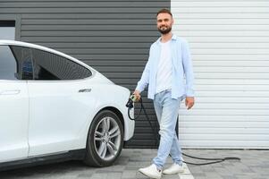 Mens Holding macht opladen kabel voor elektrisch auto in buitenshuis auto park. en hij s gaan naar aansluiten de auto naar de opladen station in de parkeren veel in de buurt de boodschappen doen centrum. foto