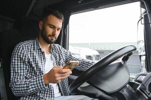 jong professioneel bestuurder communiceren over- mobiel telefoon terwijl het rijden een vrachtauto foto