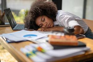 de vrouw werknemer viel in slaap Aan de bureau. uitgeput overbelasten zwart zakenvrouw vallend in slaap Aan bureaublad. moe van werk foto