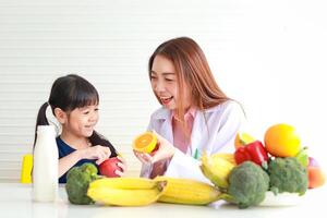 voeding voor school leeftijd kinderen. een mooi voedingsdeskundige of dokter legt uit de voordelen van fruit en groenten naar een weinig meisje. kiezen de Rechtsaf voedsel volgens naar de leeftijd van de kind. foto