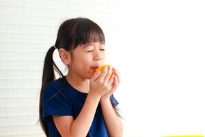 voeding voor school leeftijd kinderen. schattig weinig Aziatisch meisje geniet aan het eten sinaasappelen. kiezen de Rechtsaf voedsel volgens naar de leeftijd van de kind voor mooi zo Gezondheid foto