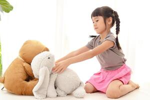schattig weinig Aziatisch meisje hebben pret ze zit met een teddy beer en een groot konijn Aan de wit bed. concept van familie, vriendschap foto