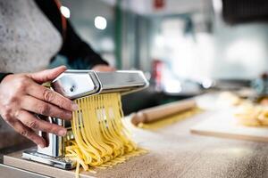 dichtbij omhoog van vrouw handen voorbereidingen treffen vers pasta gebruik makend van traditioneel machine - keuken en voedsel concept foto