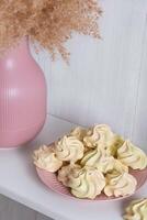 geel luchtig schuimgebak Aan een roze bord in de buurt een vaas met riet Aan een wit achtergrond foto