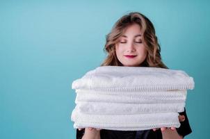Gelukkige huisvrouw die een stapel schone witte handdoeken houdt die op blauwe achtergrond worden geïsoleerd foto
