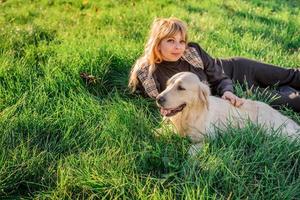 mooie blanke vrouw die in het gras ligt met haar gouden labrador retriever-hond in een park in de zonsondergang
