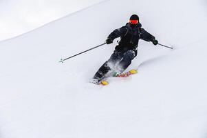 mannetje skiër bochten in los sneeuw, skiër bergafwaarts bergafwaarts Bij ski toevlucht foto