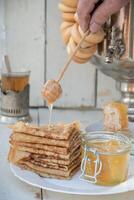 een Mens giet honing Aan pannekoeken en drankjes thee van een samovar, Russisch traditie van vieren maslenitsa foto