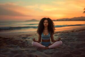 een jong zwart vrouw met lang gekruld haar- aan het doen yoga Aan de strand foto