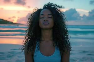 een jong zwart vrouw met lang gekruld haar- aan het doen yoga Aan de strand foto