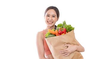 Aziatisch Japans vrouw Holding boodschappen doen zak van supermarkt vol van organische stoffen groenten en fruit voor gezond voedsel en vegetarisch salade geïsoleerd Aan wit achtergrond foto