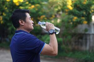 Aziatisch Mens houdt fles van drinken water naar drinken buitenshuis. concept, drinken water voor mooi zo Gezondheid. Verlichting van dorstig, en beschermen van warmte hartinfarct, koel naar beneden in heet weer voorwaarde. Gezondheid zorg. foto