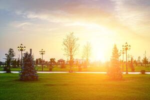 stad park in vroeg zomer of voorjaar met lantaarns, jong groen gazon, bomen en dramatisch bewolkt lucht Aan een zonsondergang of zonsopkomst. foto