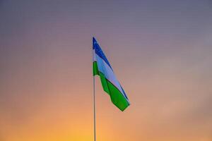 vlag van Oezbekistan golvend Aan een zonsondergang of zonsopkomst dramatisch lucht achtergrond. foto