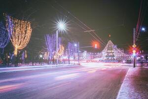 nacht winter stad met Kerstmis of nieuw jaar decoraties, net en sporen van koplampen van in beweging auto's. wijnoogst film stijlvol. foto