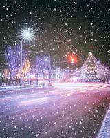 nacht winter stad met Kerstmis of nieuw jaar decoraties, net en sporen van koplampen van in beweging auto's in een sneeuwval. wijnoogst film stijlvol. foto