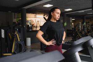 portret van een vrouw resting na haar training. ze is leunend Aan een loopband en looks helemaal uitgeput foto