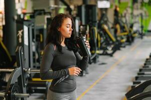 jong mooi vrouw drinken water in sport- Sportschool. foto