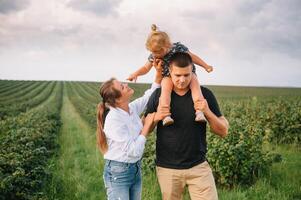 gelukkig familie wandelen in de park. mama, vader en dochter wandelen buitenshuis, ouders Holding de baby meisjes handen. jeugd, ouderschap, familie obligaties, huwelijk concept. foto