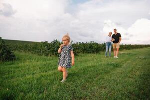 gelukkig familie wandelen in de park. mama, vader en dochter wandelen buitenshuis, ouders Holding de baby meisjes handen. jeugd, ouderschap, familie obligaties, huwelijk concept. foto