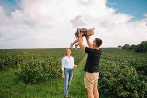 gelukkig familie wandelen in de park. mama, vader en dochter wandelen buitenshuis, ouders Holding de baby meisjes handen. jeugd, ouderschap, familie obligaties, huwelijk concept. foto