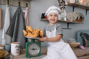 jong jongen schattig Aan de keuken koken chef in wit uniform en hoed in de buurt tafel. eigengemaakt ontbijtkoek. de jongen gekookt de chocola koekjes. foto