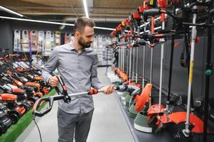 gelukkig klant met elektrisch gazon trimmer in handen Bij tuin uitrusting op te slaan foto