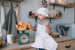jong jongen schattig Aan de keuken koken chef in wit uniform en hoed in de buurt tafel. eigengemaakt ontbijtkoek. de jongen gekookt de chocola koekjes. foto