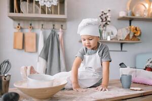 jong jongen schattig Aan de keuken koken chef in wit uniform en hoed in de buurt tafel. eigengemaakt ontbijtkoek. de jongen gekookt de chocola koekjes. foto