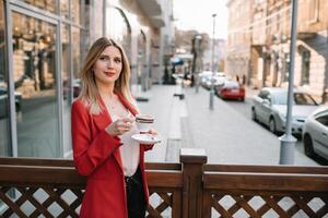 mooi jong zakenvrouw met een beschikbaar koffie beker, drinken koffie, en Holding tablet in haar handen tegen stedelijk stad achtergrond foto