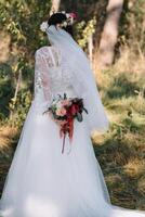 bruid staat in een wit bruiloft jurk met een boeket van bloemen. foto