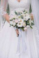 bruid staat in een wit bruiloft jurk met een boeket van bloemen. foto