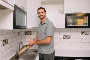 Mens snijdend vers vis in keuken in huis. Mens slachten vis voor koken. foto