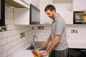 Mens snijdend vers vis in keuken in huis. Mens slachten vis voor koken. foto