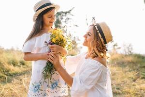 vrolijk moeder en haar weinig dochter hebben pret samen in de zomer achtergrond. gelukkig familie in de natuur achtergrond. schattig meisjes met kleurrijk bloemen. foto